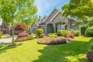 beautiful stone home with a green lawn, trees, and bushes